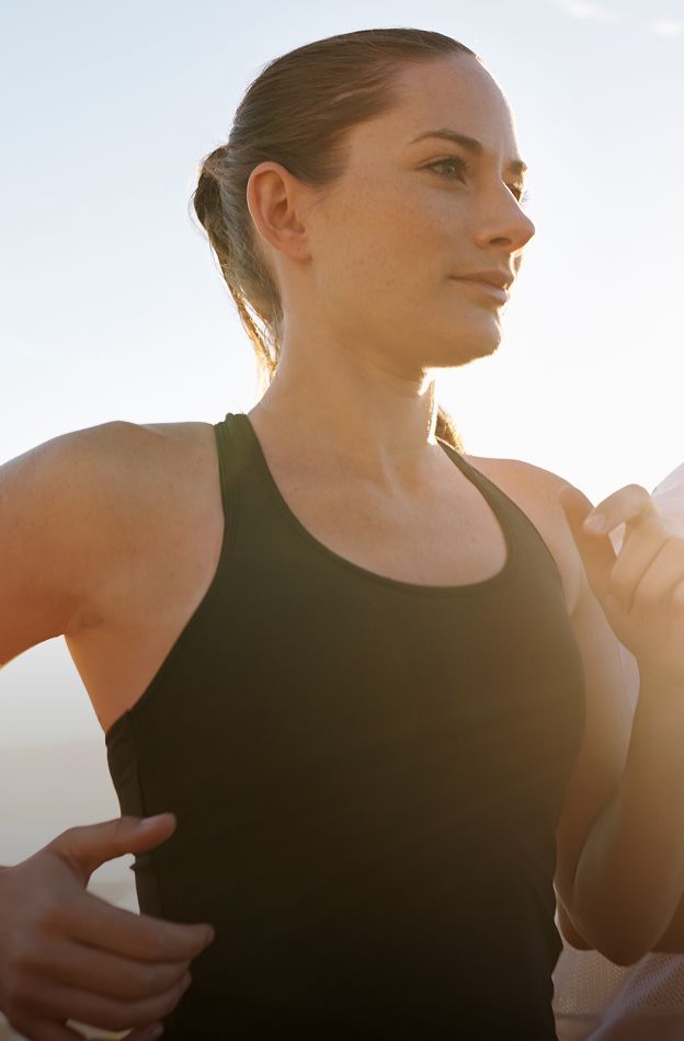 Woman jogging in sunlight, focused expression.