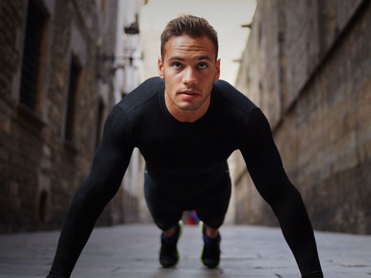 Man doing push-ups in urban alleyway.