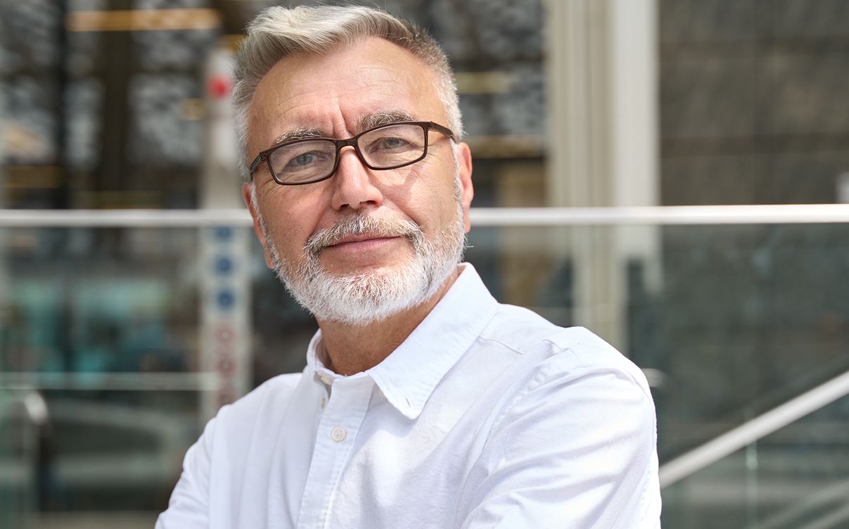 Older man with glasses smiling outdoors.
