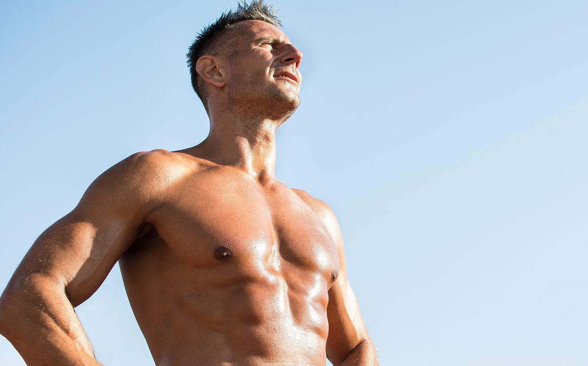 Muscular man standing confidently under blue sky.